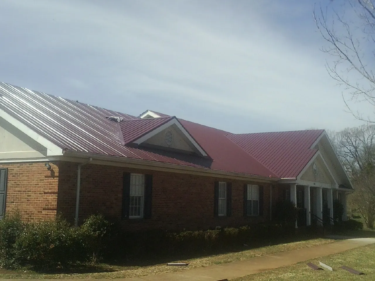 Red metal roof with gabled entries on a long brick building, from a Hail Damage Roof Repair job in Lynchburg